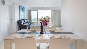 A modern dining area with a glass table, white chairs, and a vase of flowers. - Kata Ocean View 2BR Apartment O910 (Karon)