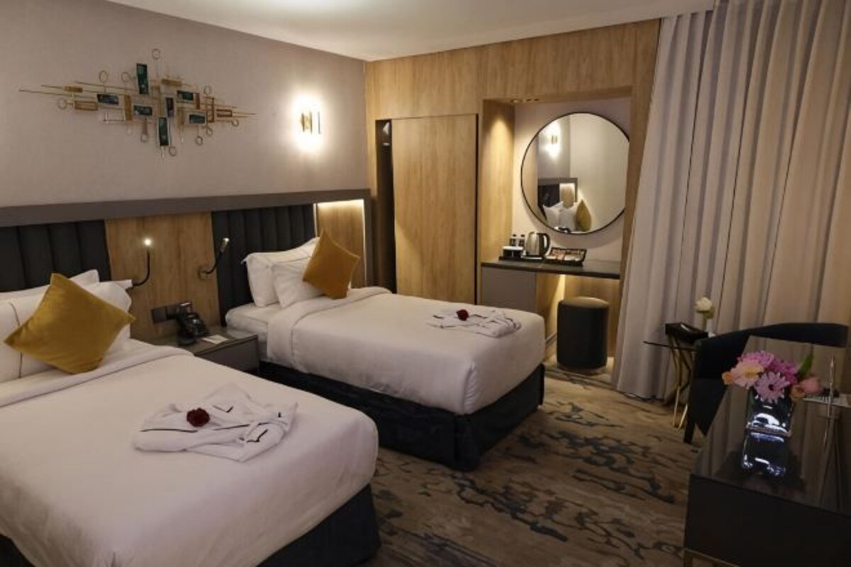 A hotel room with two beds, a desk, a mirror, and a small sitting area.