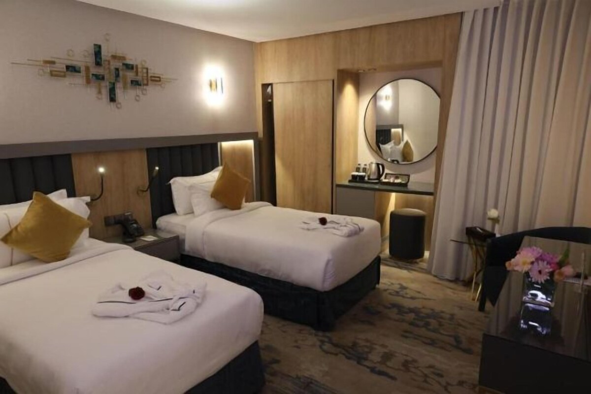 A hotel room with two beds, a desk, a mirror, and a bathroom.