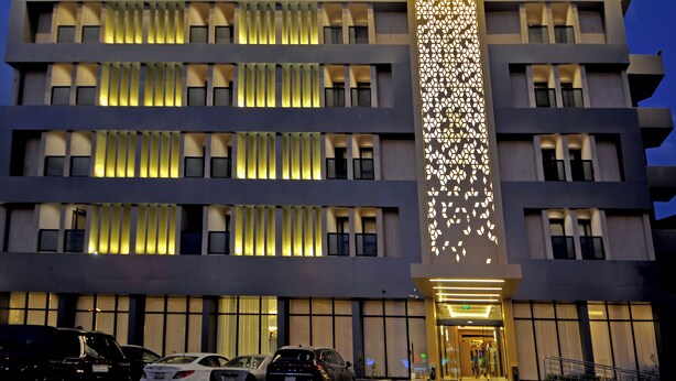 A multi-story hotel with a modern facade, illuminated signage, and a central vertical light feature. - AW Hotel Riyadh (Riyadh)