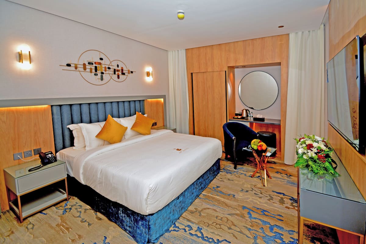 A hotel room with a large bed, bedside table, nightstand, and a mirror.