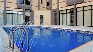 A swimming pool with clear blue water, surrounded by a beige building with large windows and balconies. - AW Hotel Riyadh (Riyadh)