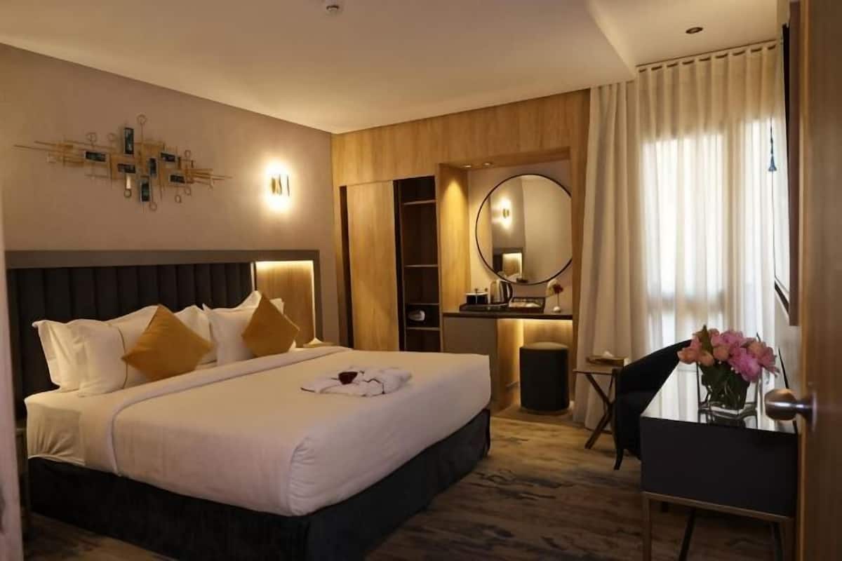 A hotel room with a large bed, bedside table, mirror, and a desk with a chair.