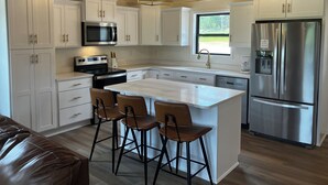 Een moderne keuken met witte kasten, een roestvrijstalen koelkast, een inbouwoven en een bar met krukken.