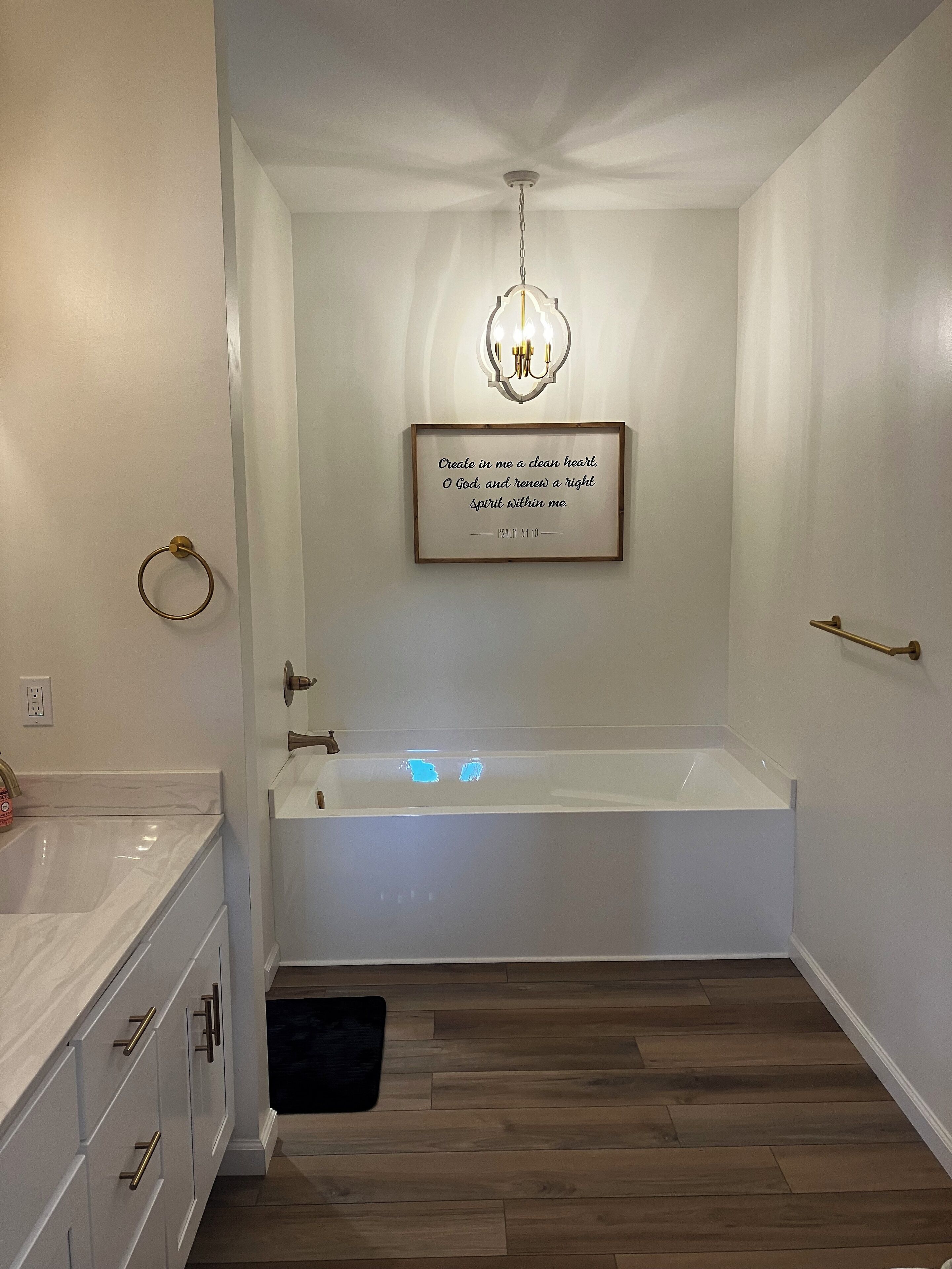 A modern bathroom with a white bathtub, a wooden floor, and a wall-mounted light fixture.