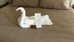 Een bed met een handdoek in de vorm van een zwaan en een kaartje met de tekst 'YOU ARE LOVED' op een bruine sprei.