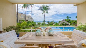 A balcony with a table, chairs, and a view of a pool and palm trees.