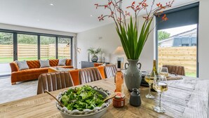 Un comedor moderno con una mesa de madera, un tazón de ensalada, una botella de vino y un jarrón de flores.