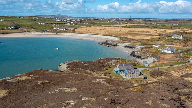 Un paisaje costero con una playa de arena, un litoral rocoso y algunas casas.