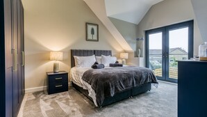 Un dormitorio con una cama grande, dos mesitas de noche con lámparas, un cuadro enmarcado en la pared y vistas amplias por una ventana grande.
