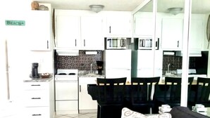 Un espacio habitable compacto con kitchenette, un sofá con cojín estampado y piso de baldosas.