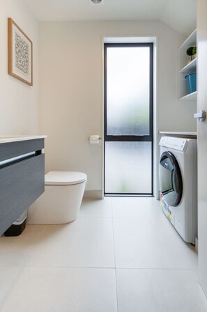 A compact, modern bathroom with a toilet, a washing machine, and a grey cabinet.