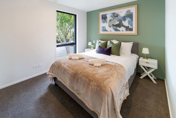A bedroom with a large bed, a window with a view of trees, and a painting on the wall.