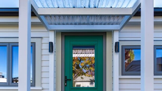 A modern house with a green door, a wooden front porch, and a pergola with a white roof.