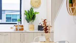 Una cucina moderna con mobili in legno, un piano di lavoro bianco e un tavolo rotondo con sedie. Si vede un orologio appeso al muro e una pianta in vaso sul piano di lavoro.