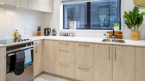 Una cucina moderna con mobili chiari in legno, un forno in acciaio inossidabile, una finestra con vista e una pianta in vaso sul piano di lavoro.
