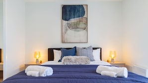 A neatly made bed with a blue bedspread, two pillows, and two bedside lamps.
