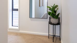 A hallway with a large mirror, a potted plant, and a window with blinds.