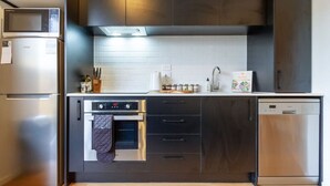 Een moderne keuken met een roestvrijstalen koelkast, oven en vaatwasser, donkere kastjes en een witte betegelde achterwand.