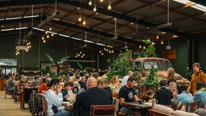 Een levendige eethoek binnenshuis met tafels, stoelen, hanglampen en een verzameling klassieke auto's.