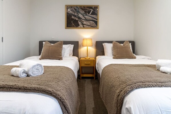A hotel room with two beds, a nightstand with a lamp, and a painting on the wall.