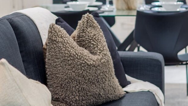 Una sala de estar moderna con un sofá gris oscuro, dos almohadones con textura y un jarrón con flores secas.
