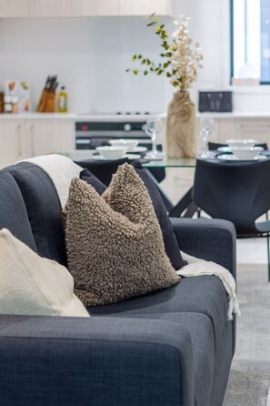 Una sala de estar moderna con un sofá gris oscuro, dos almohadones con textura y un jarrón con flores secas.