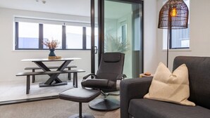 Una sala de estar moderna con un sofá, una butaca negra, una mesa de comedor y una lámpara de pie.