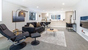 Una sala de estar moderna con un sofá, sillones y una mesa de centro. Se observa una cocina al fondo con una zona de comedor.