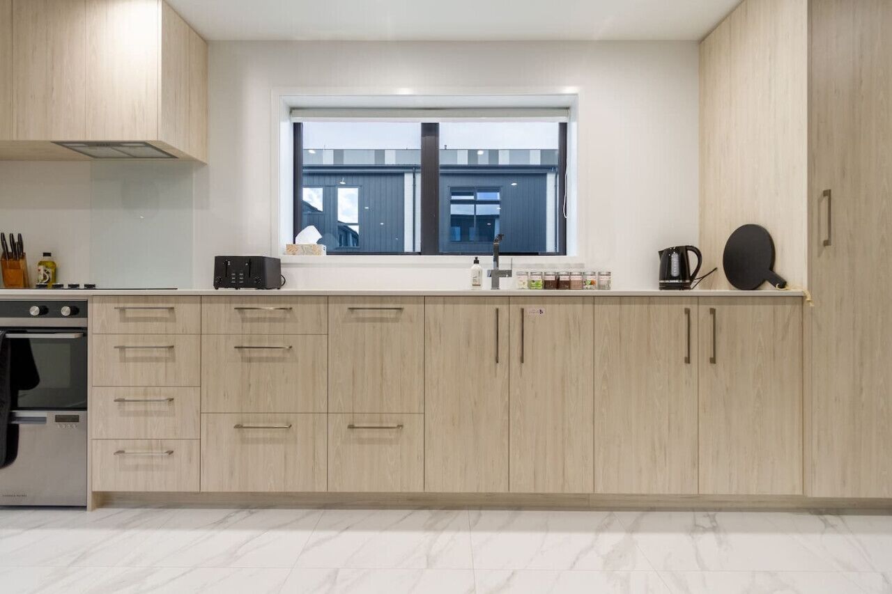 A modern kitchen with light wood cabinets, a built-in oven, and a window with a view of buildings outside.
