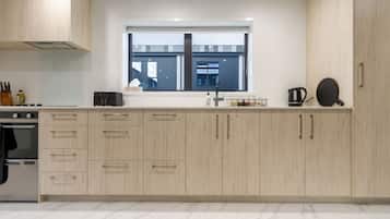 A modern kitchen with light wood cabinets, a built-in oven, and a window with a view of buildings outside.