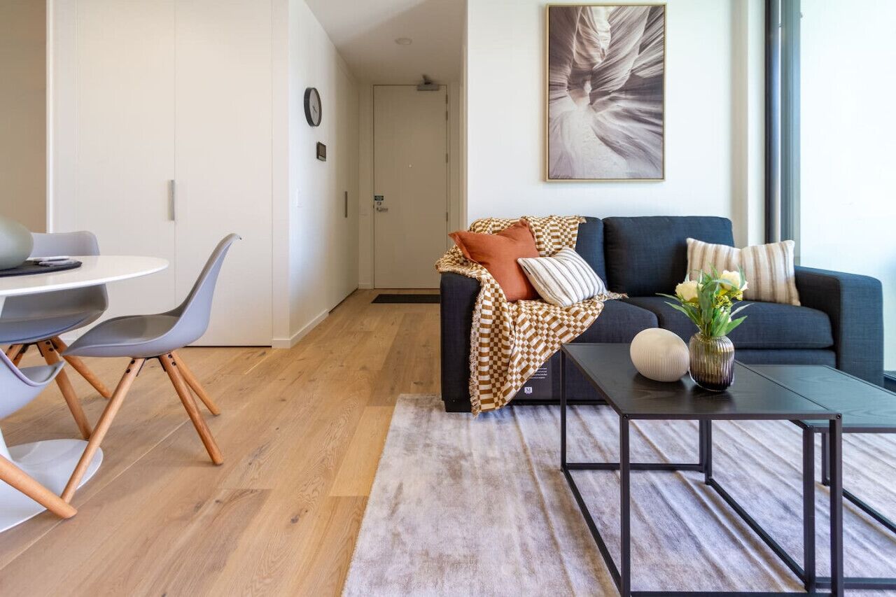 A modern living room with a dark blue sofa, a round coffee table, and a dining area with a white table and grey chairs.