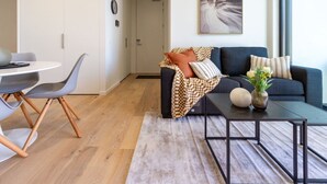 Una sala de estar moderna con un sofá azul oscuro, una mesa de centro redonda y un comedor con una mesa blanca y sillas grises.