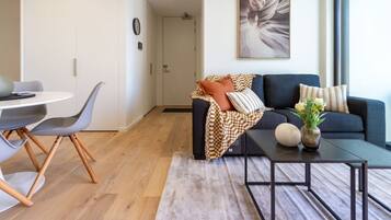 A modern living room with a dark blue sofa, a round coffee table, and a dining area with a white table and grey chairs.