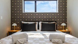 Un letto matrimoniale con copriletto trapuntato, due comodini con lampade, una finestra con vista e una parete decorata.