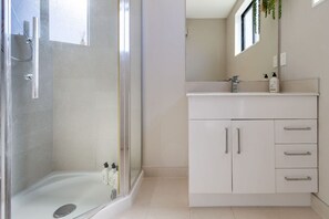 A modern bathroom with a glass-enclosed shower, a white vanity with a mirror, and a window providing natural light.