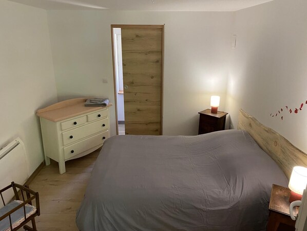 Quarto com uma cama grande, uma porta de madeira, uma mesa de cabeceira com abajur e uma cadeira pequena.