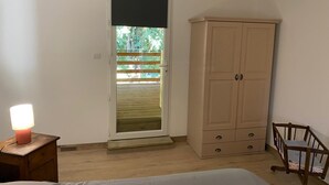 Un dormitori amb llit, un armari, una nit abill amb una làmpada i una finestra que dona a vistes de vegetació.