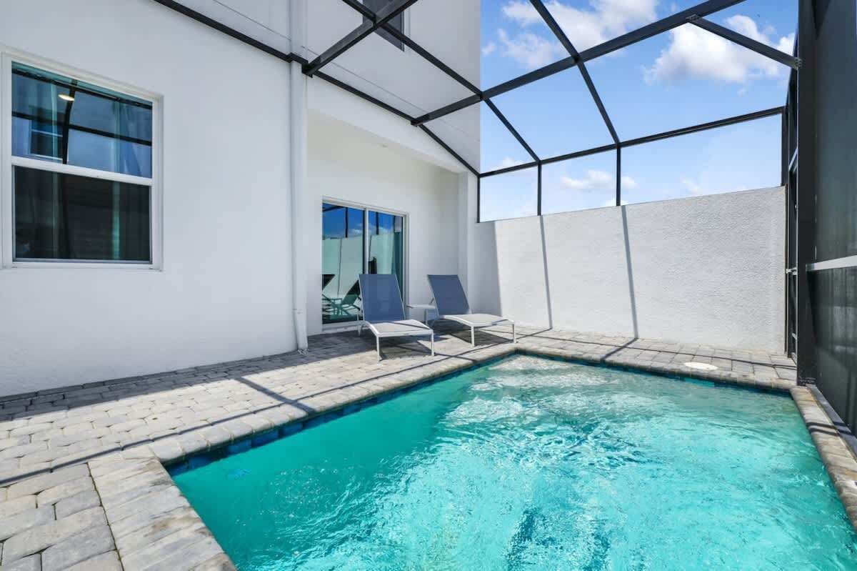 A swimming pool with a clear blue water, surrounded by a white wall and a glass enclosure.