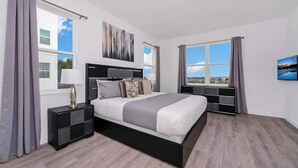 Quarto moderno com cama grande, mesa de cabeceira, criado-mudo e janela com cortinas.