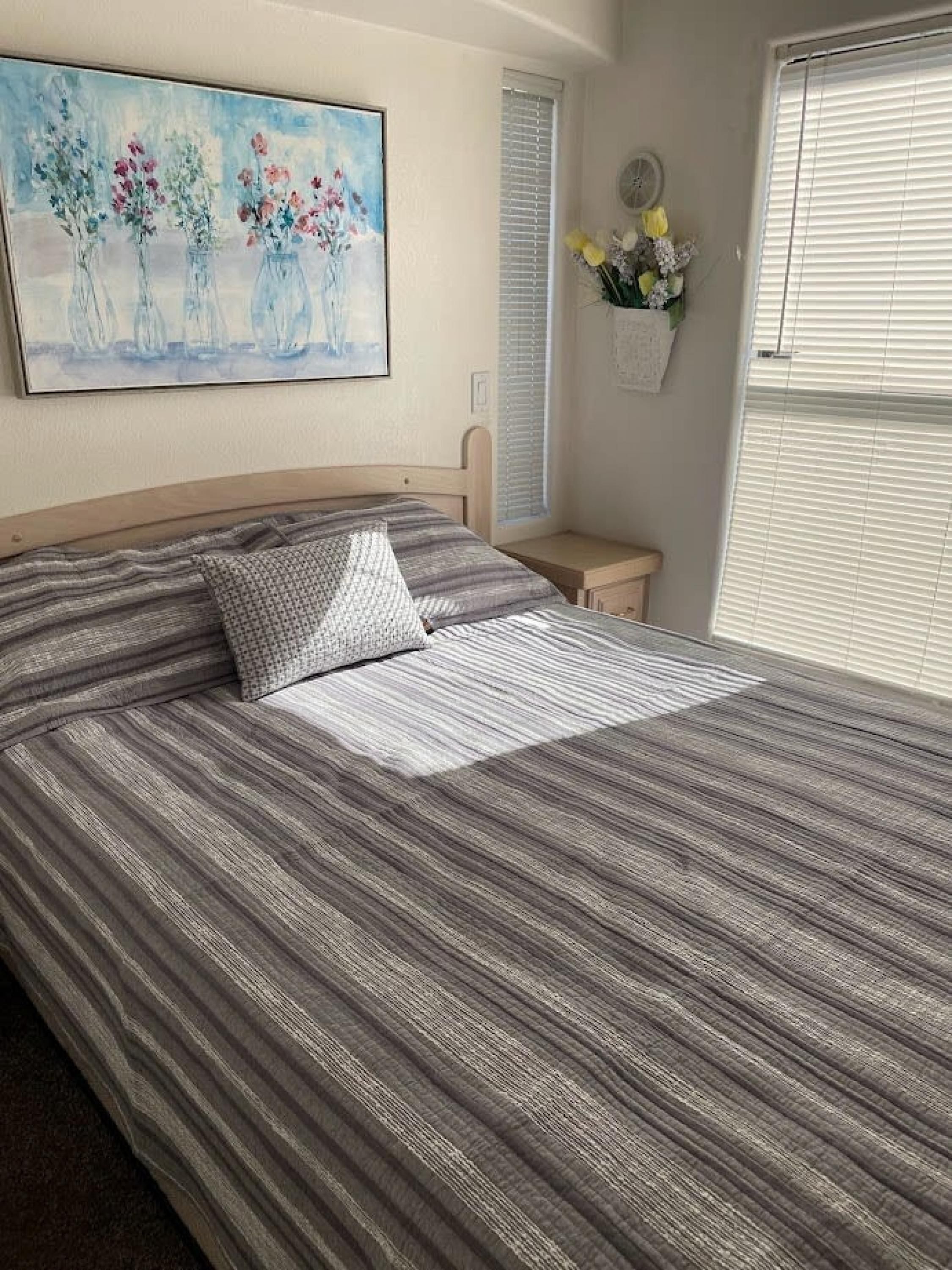 A neatly made bed with striped bedding, a pillow, and a small bedside table with a vase of flowers.
