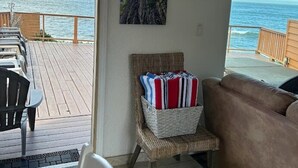 A room with a view of the ocean, a wicker chair with cushions, a brown sofa, and a dining area with chairs and a table. - Ocean Front Cabin 16 Jacuzzi Incredible Views (Smith River)