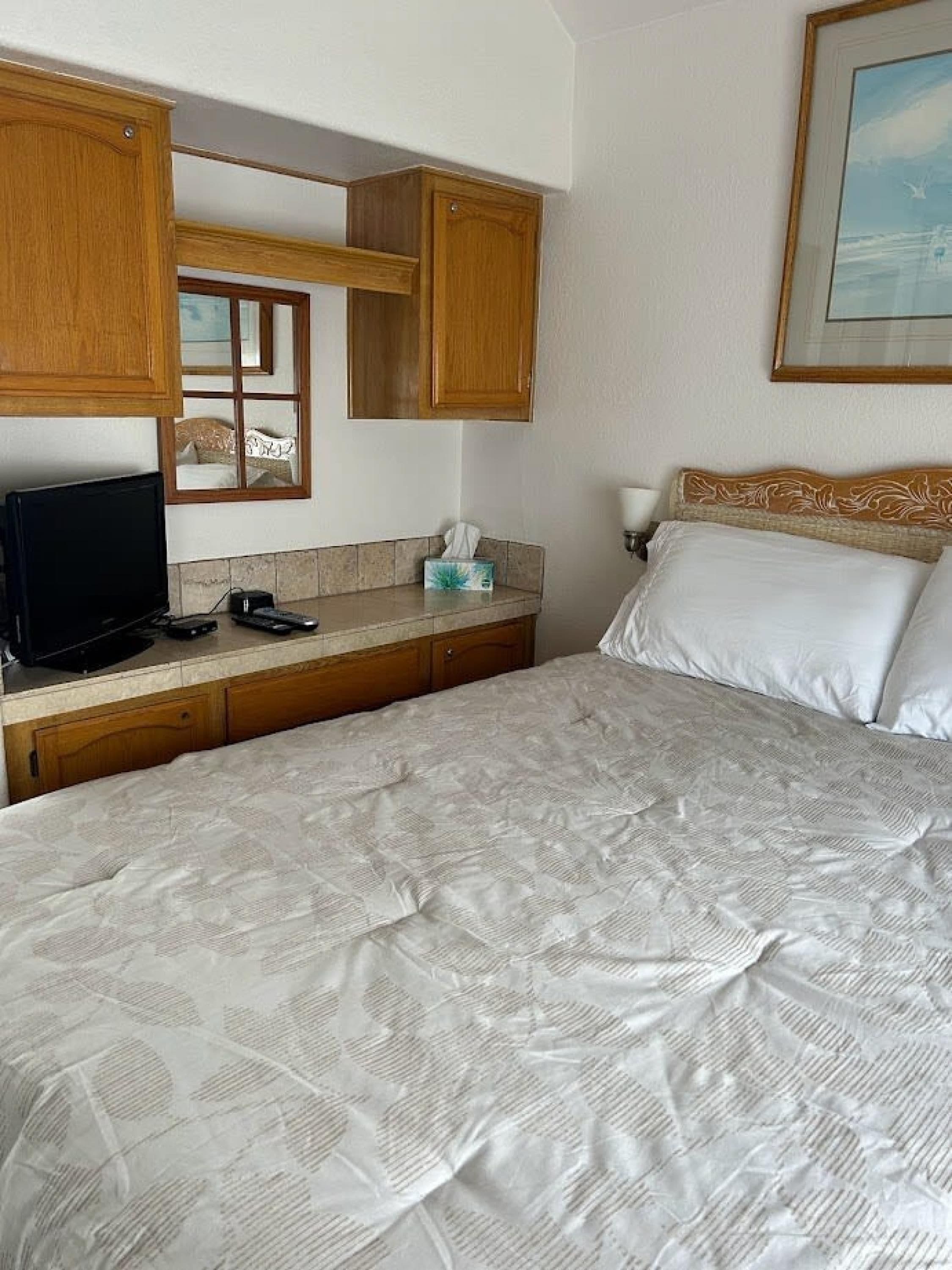 A hotel room with a bed, a desk with a laptop, a telephone, and a window with a view of the beach.