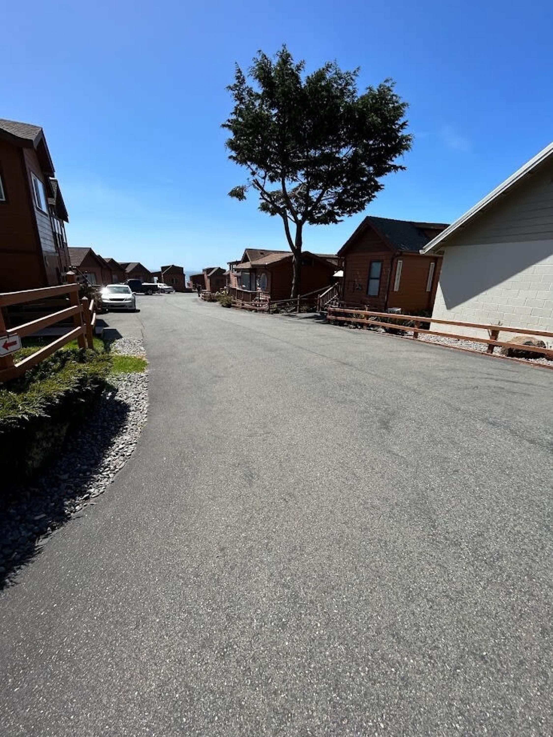 A street lined with single-story wooden houses, a clear sky, and a parked car.