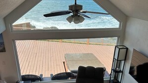 A living room with a large window overlooking the ocean, a ceiling fan, a sofa, a chair, and a wooden coffee table. - Ocean Front Cabin 16 Jacuzzi Incredible Views (Smith River)