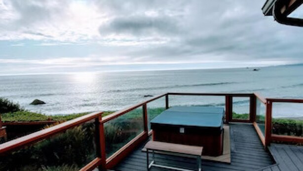 Terraza de madera con mesa y banco con vistas a un cuerpo de agua.