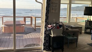 Un interior acogedor con un amplio ventanal con vista al océano, una terraza de madera y una zona de estar confortable.