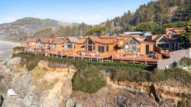 Une rangée de cabanes en bois dotées de balcons, situées sur une côte rocheuse, avec une colline boisée en arrière-plan.