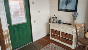 Une pièce avec une porte verte, une commode blanche avec des paniers, une petite table et un tableau encadré au mur.