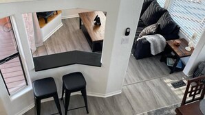 A modern kitchen with a black countertop and two stools, a dining area with a wooden table and chairs, and a cozy seating area with a sofa and cushions. - Oceanview Cabin 22 w Jacuzzi Wonderful View (Smith River)